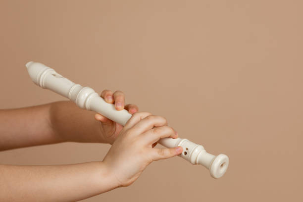 fipple flöte mit beiden händen halten und löcher in nahaufnahme drücken, beiger hintergrund. holzblasinstrument. - flute solo stock-fotos und bilder