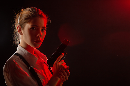 serious young woman with gun in dark looking at camera toned image with copy space