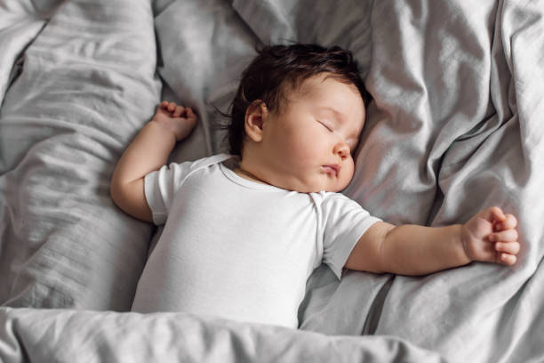 portrait of baby in sleepwear lying under gray blanket on bed at home. sleeping on back infant child in bedroom, see sweet dream. grey background, free copy space. childcare and healthy sleep concept - 嬰兒 圖片 個照片及圖片檔