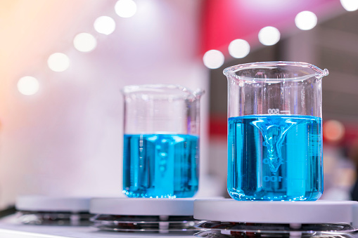 Close up of beautiful vortex blue colorful chemistry liquid in beaker laboratory glass flask on magnetic stirrer or mixer machine for science