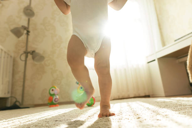 Little boy in bodysuit walking on a floor in his bedroom. Little boy wearing bodysuit is making his first steps on a carpet covered floor in his bedroom. first steps stock pictures, royalty-free photos & images