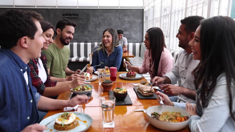 Happy group of Latin American friends eating together at a restaurant while talking and laughing