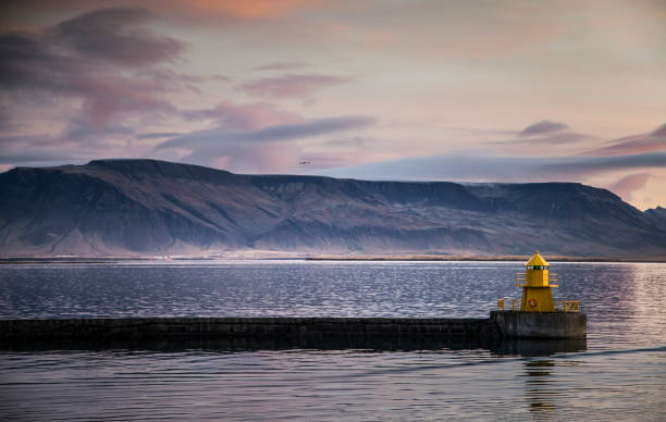 Panoramic view of the Norwegian Sea at sunset with mountains in the background and a yellow lighthouse in the foreground.