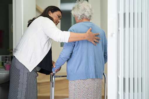 El cuidador ayuda a una anciana asiática o anciana a caminar con el apoyo de un andador por las escaleras de la casa. photo