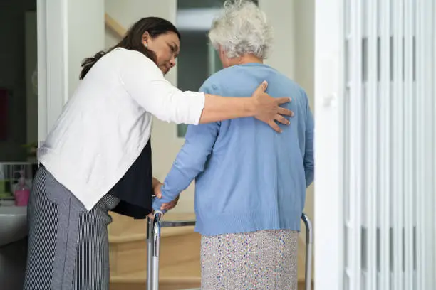 Photo of Caregiver help asian or elderly old woman walk with walker support up the stairs in home.