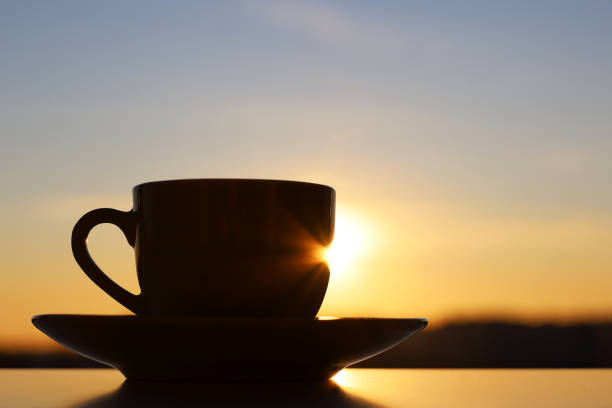 istock Silhouette of coffee or tea cup on sunrise sky background 1383513171
