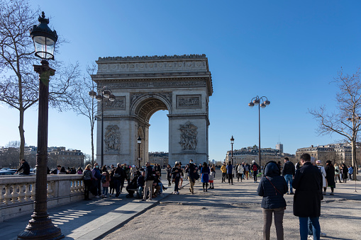Champs Elysees and Arc de Triomphe in late afternoon sun with tourists in the foreground in Paris, France, Europe.