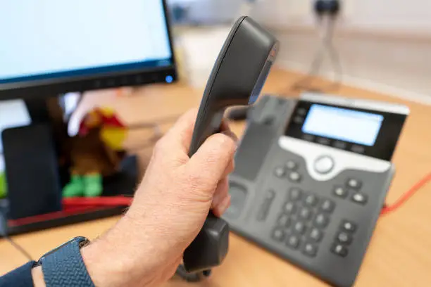 Photo of Helpdesk employee seen picking up a phone call using a VoIP desk phone.