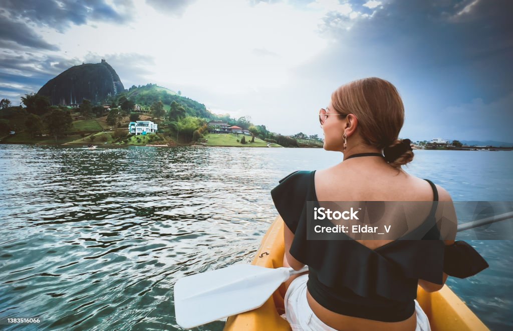 Latina woman traveling in a kayak Latina woman in green dress, traveling in a kayak on a lake and in the background you can see a mountain and a lake house. Lake Stock Photo
