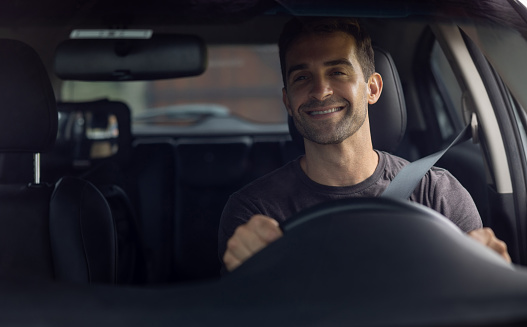 Portrait of handsome smiling latin man driving a car. Car sharing concept