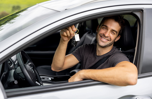 Portrait of a happy Brazilian man sitting in his new car and holding the keys while looking at the camera smiling