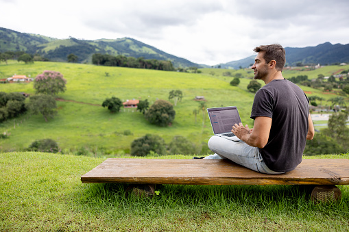 Happy Brazilian man working online at the countryside using a laptop computer. **IMAGE ON SCREEN BELONGS TO US**