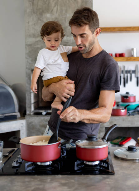 homem cozinhando o jantar em casa enquanto cuidava do filho - stay at home dad - fotografias e filmes do acervo
