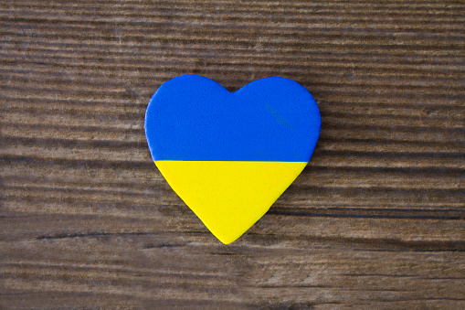 A heart shape in the colours of the Ukrainian flag, on a  rustic  wooden background.