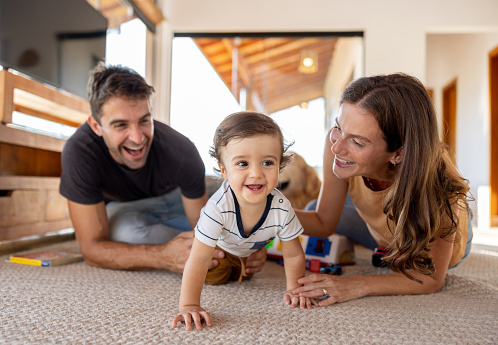 Happy Brazilian parents watching their son crawling at home and smiling - family concepts