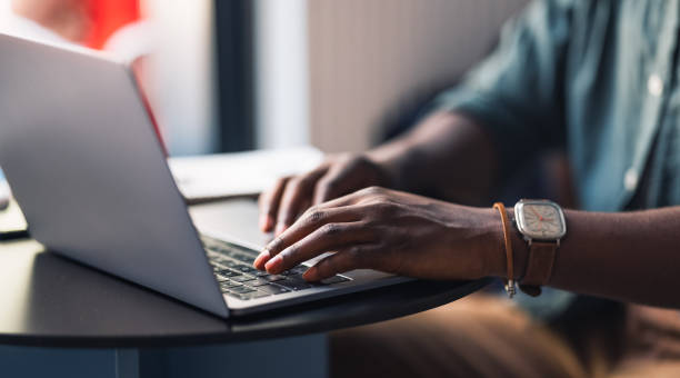 An Anonymous Student Using his Laptop Computer in a Cafe Close up photo of unrecognizable African-American man hands typing homework on his laptop keyboard while sitting in a coffee shop. black man laptop stock pictures, royalty-free photos & images