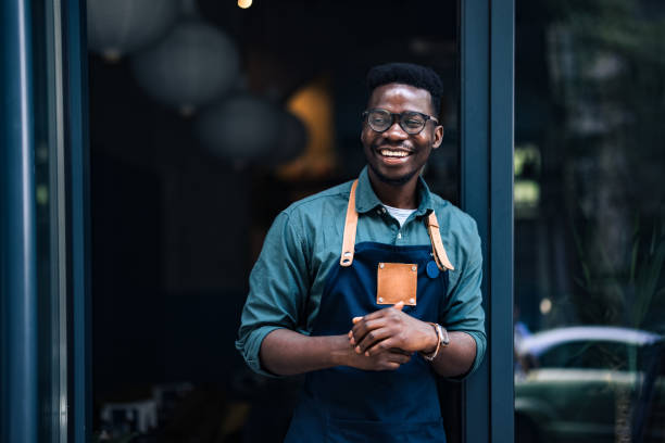 ritratto di un uomo felice e fiducioso in piedi sulla porta del suo bar - owner small business restaurant african ethnicity foto e immagini stock