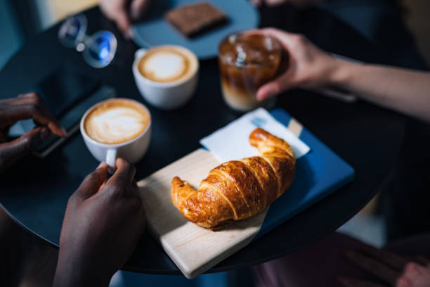 Unrecognizable Male and Female Friends Having Coffee and Breakfast in a Coffee Shop Close up photo of anonymous multi ethnic friends sitting at table together, drinking cappuccino and iced coffee with breakfast in a cafe. croissant stock pictures, royalty-free photos & images