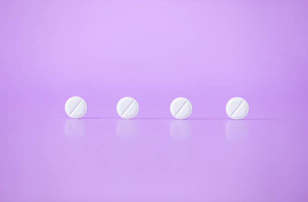 White pills, medical tablets, placebo or vitamins on purple background closed up, horizontal plane. Pill is a medicinal substance in a small round or oval mass meant to be swallowed. it travels through the stomach and small intestine into the liver, which breaks it down and releases the remnants into the blood stream statin photos stock pictures, royalty-free photos & images