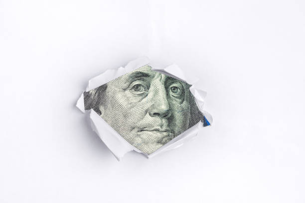 istock Benjamin Franklin peers through white torn paper. 1383528433
