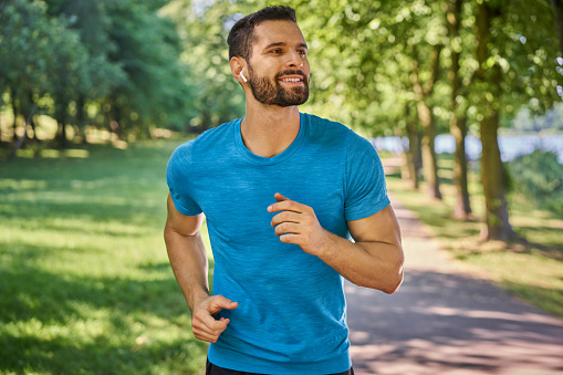 Hombre feliz corriendo en el parque escuchando música con auriculares en un día soleado de verano photo