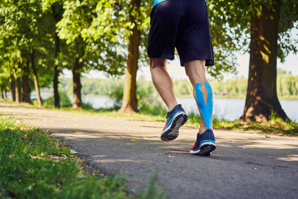 Man with kinesiology tape running in park during sunny summer day stock photo