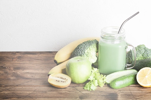fresh green smoothie in glass bottle with vegetables on wooden and white background.vegan food, self care and healthy lifestyle.Healthy detox diet