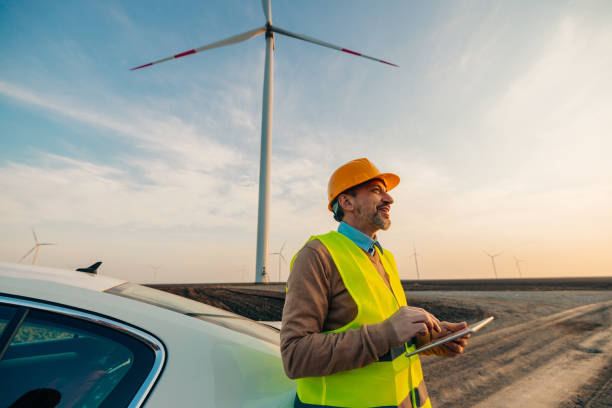 istock Smiling engineer standing by car on a wind farm 1383538417