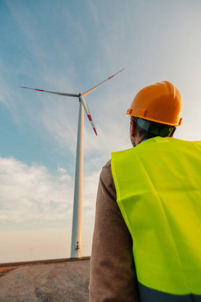 istock Engineer standing in field with wind turbines 1383538427