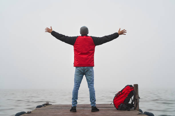 liberdade e conceito de sucesso. jovem com mochila vermelha abre braços para vasto oceano em doca de madeira - solitary confinement - fotografias e filmes do acervo