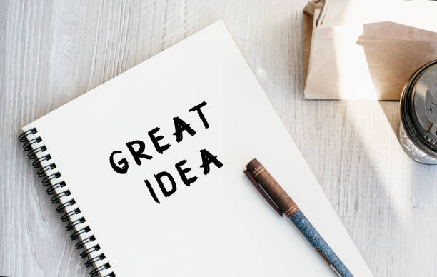 istock Notepad with the inscription GREAT IDEA. Paper cup with coffee and paper bag with breakfast on the table. View from above. Marketing concept. 1383548009