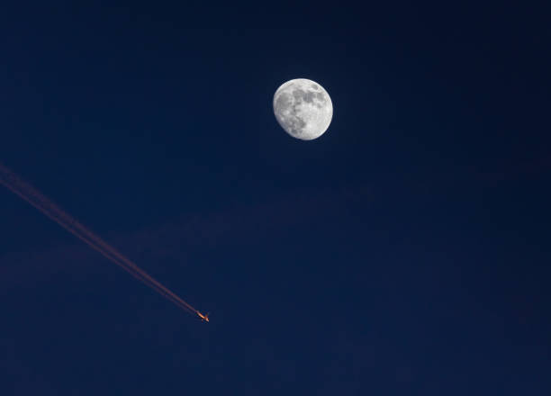 Airplane passing by waxing Moon on blue sky Closeup of the waxing moon and an airplane passing close by, leaving a contrail which is illuminated by the setting sun - - early evening capture against dark blue sky. Stuttgart, Germany January 22, 2022 contrail moon on a night sky stock pictures, royalty-free photos & images