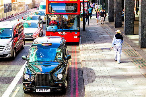 London, UK - June 22, 2018: High angle view road street above black taxi cab vehicle in traffic jam at Waterloo train station with people pedestrians walking on sidewalk pavement