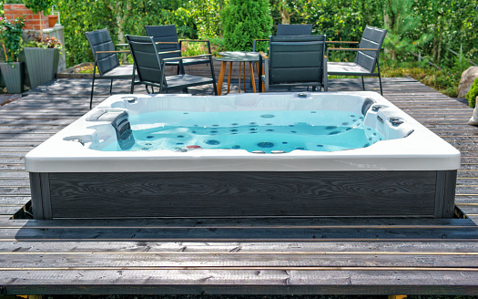 Large hot tub embedded in the backyard terrace. A sunny summer's day in the shelter of a green garden. Everyday luxury and relaxation in your own backyard. Spa complex, vacation and traveling concept.