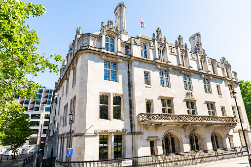 London, UK - June 22, 2018: Supreme Royal Courts of Justice facade exterior architecture in center of downtown city in summer on Broad Sanctuary Street with Union Jack flag