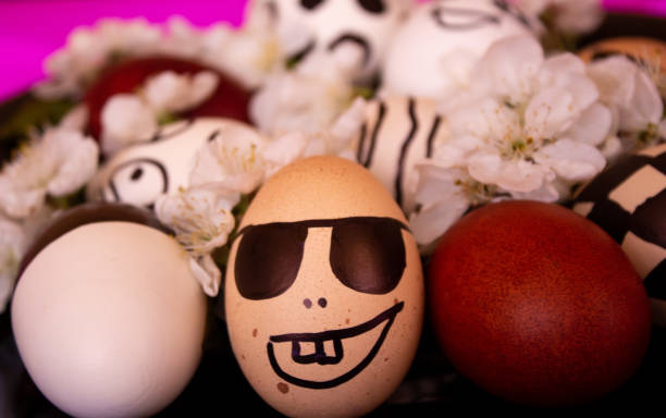 istock Funny Easter eggs with painted emoticons and white flowers next to them. Celebration. Easter egg with painted black glasses and a smile. Easter with your own hands. Minimal easter holiday concept 1383569823