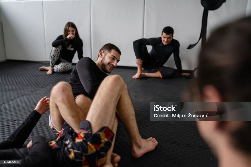 two men demonstrate bjj brazilian jiu jitsu grappling or luta livre technique on the ground at training at the academy in front of group of students leg attack Brazilian Jiu-Jitsu Stock Photo