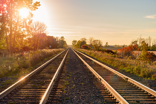 Two parallel railway tracks running through agricultural fields in the countryside at sunset in autumn. Lens flare.