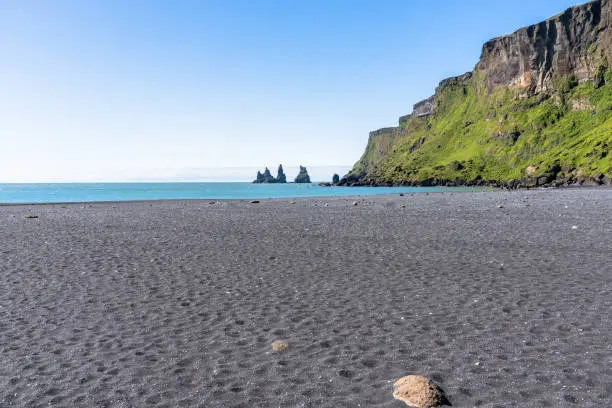 Beautiful black-sand beach with people horseback riding in distance on a clear summer morning. Vik, Iceland.