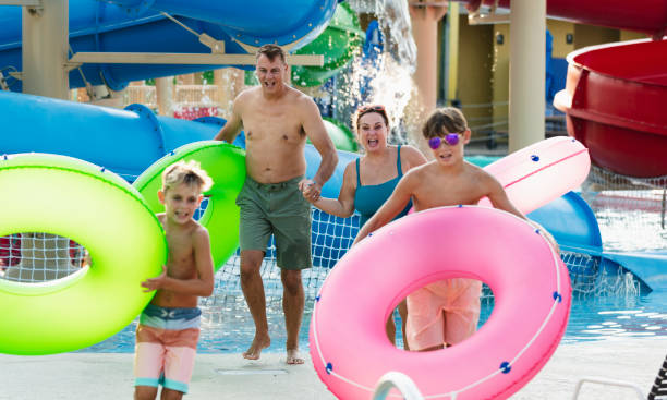 семья в аквапарке несет надувные кольца к ленивой реке - water park inflatable ring water swimming pool стоковые фото и изображения