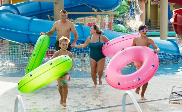 A multiracial family with two children having fun at a water park. The boys are 9 and 12 years old. Mom is Hispanic and dad is Caucasian. They are carrying inflatable rings, ready to float on the lazy river.