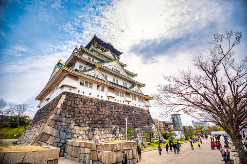 Osaka, Japan - March 28, 2019 : Low angle view of Osaka castle and tourist people in spring before cherry blossom in a public park