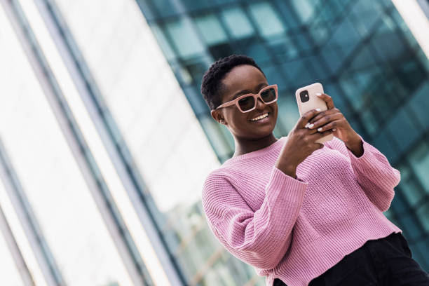 istock Beautiful young black business woman smiling while using her phone outside 1383603131