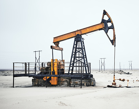 Oil frozen pump on sand field, cloudy gray sky