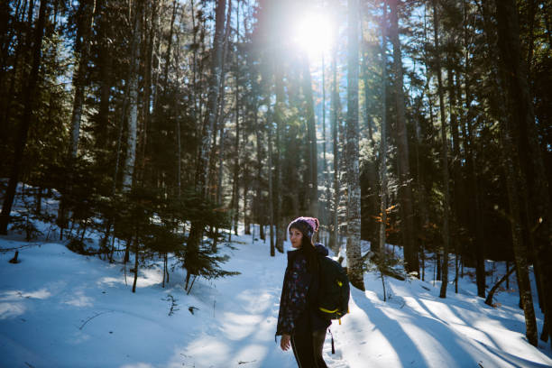 Woman enjoying the nature trip in the snowy mountain forest. She is snowshoeing on a lovely and sunny winter day.