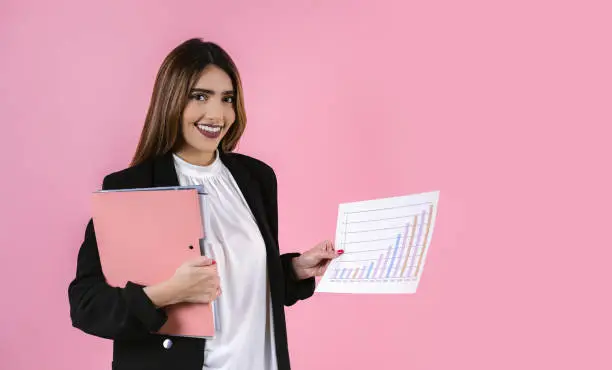 Photo of young hispanic business woman holding statistics graph and smiling at camera on pink background in Mexico Latin America