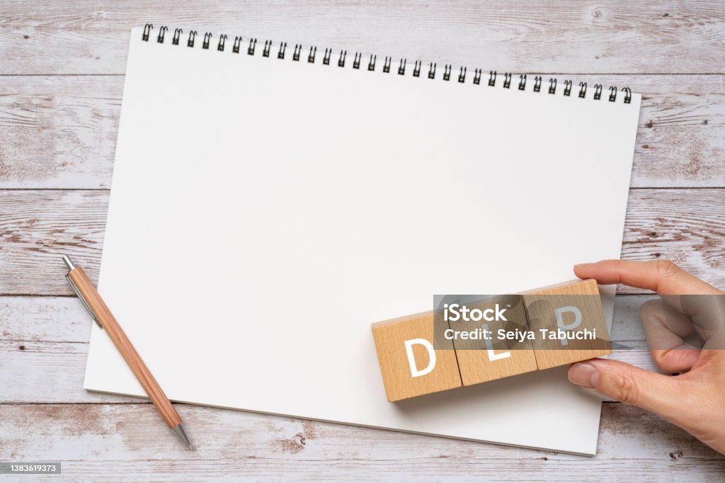 Wooden blocks with "DLP" text of concept, a pen, a notebook, and a hand. Backup Stock Photo