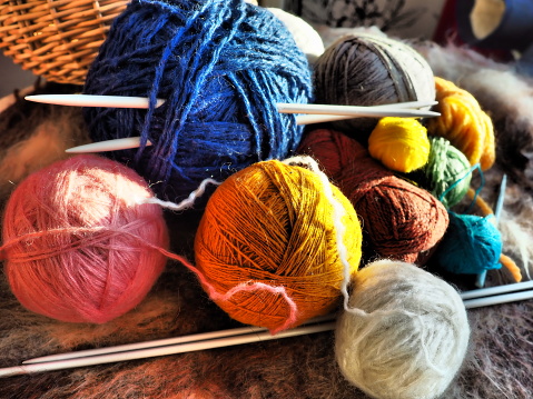 Knitting a scarf or sweater from gray, blue, white and orange yarns. Hanks of woolen and acrylic threads. Knitting as a hobby. Accessories, knitting needles, crochet hooks