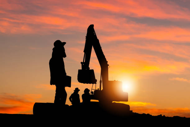 istock Silhouette of Foreman and workers team at construction site, Road construction worker and excavator with blurred sunset background 1383626667