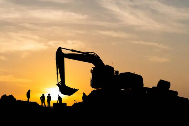 Photo of Silhouette of Foreman and workers team at construction site, Road construction worker and excavator with blurred sunset background